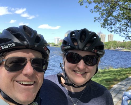 Woody Pollack & Dineen Wasylik wearing bike helmets in front of the Boston skyline